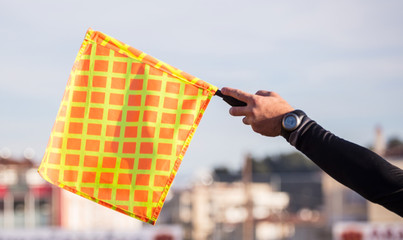 Soccer referee assistant raises the flag with his hand. Blur blue sky and buildings background,...