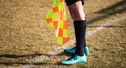 Soccer referee assistant stands at sideline with flag at hands. Blur green field background, close...