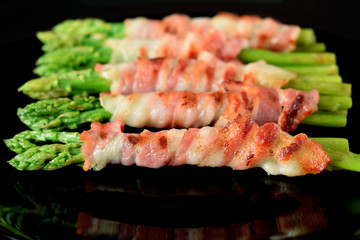 Green asparagus wrapped into smoked bacon on a black plate