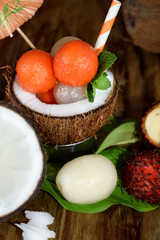 Tropical fruits: longan, rambutan and papaya ball-shaped pieces in a coconut. Cocktail ingredients