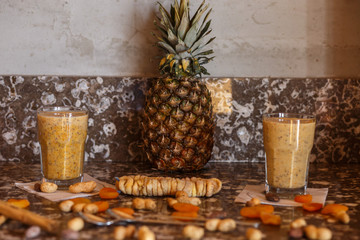 two glasses of  yellow smoothie and ananas, figs, dried apricots on the marble table in the kitchen 