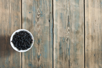 Black raisins in bowl over wooden background.