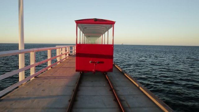POV view from behind of vintage red train illuminated by sunset light, going on Jetty Busselton tracks in Busselton town, WA. Busselton Jetty is the longest wooden pier in the world and iconic place.