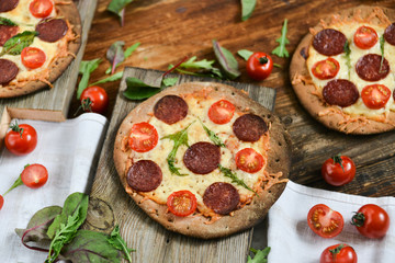 Mini Pizza With Cherry Tomatoes And Salami Sausages On A Wooden Background Natural Rustic, A Pizza Cutter And Ingridienty.
