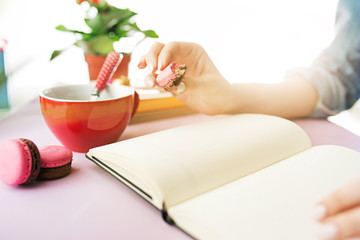 The female hands holding french macarons on trendy pink desk.