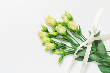 Bouquet of fresh unblown white bud in flowers on a light background with copy space. Bunch of young white roses with ribbon. Top view.