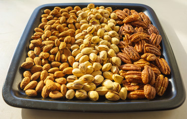 Nuts almonds, pistachios and pecans on black plate, close-up, set.  