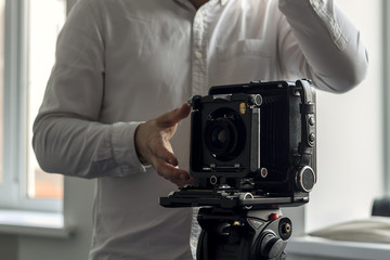 The old camera on a tripod stands on a background of a wall