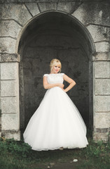 Obraz premium Beautiful elegant bride with perfect wedding dress and bouquet posing near old castle