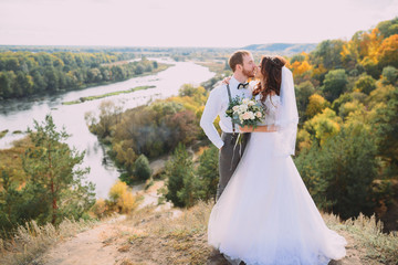 Fototapeta na wymiar Stylish bride and groom posing on the background of the river. Wedding couple