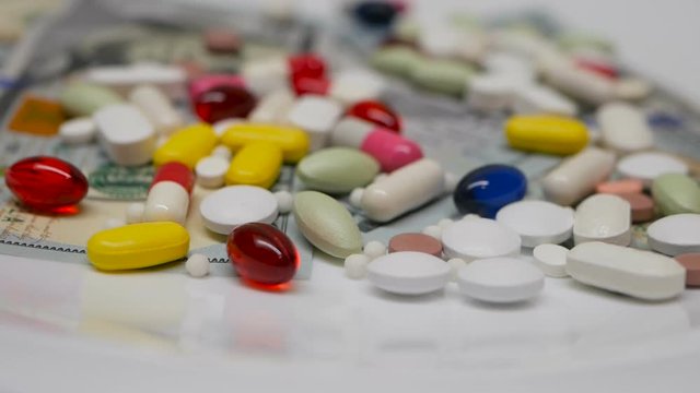 Dollars and colourful pills turning against white background