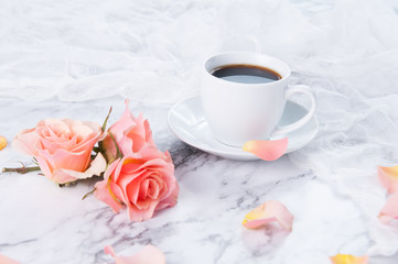 cup of coffee on a marble counter top with peach colored roses
