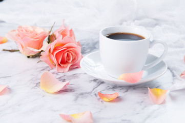 Fototapeta na wymiar cup of coffee on a marble counter top with peach colored roses