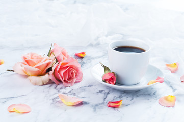 Fototapeta na wymiar cup of coffee on a marble counter top with peach colored roses