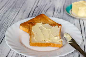 Still life with bread and butter in a white plate on a wooden background