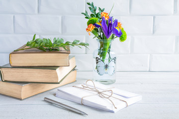 Old books and envelopes, a vase of flowers against a white brick wall.