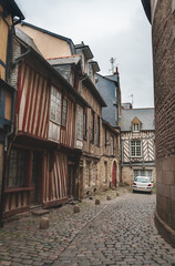 Narrow cobblestone alley with historic half-timbered houses and modern cars in old city center of Rennes, Brittany, France