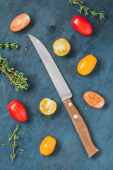 Top view of colorful cherry tomatoes and a knife on a blue table. Flat lay.
