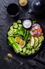 Fototapeta na wymiar Healthy salad with fresh cucumber,celery,watercress,carrot,radish,green apple,kiwi and boiled egg on black plate.Top view,close-up