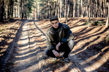A guy in a leather jacket and cap on a road in a pine forest