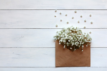 Gipsofila flowers in a paper envelope on a white wooden background