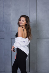 Portrait of a young smiling woman on a gray wall background. A beautiful girl in white shirt and black lingerie stands near a concrete wall