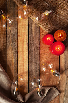 Top view image with bulblight garland, glowing candles and sackcloth bag on raw rustic background.