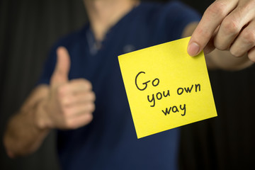 Man holds yellow sticker inscription . Thumb up Blue T-shirt. close-up, selective focus