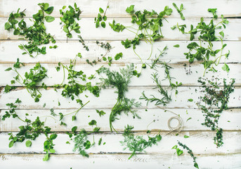 Flat-lay pattern of bunches of fresh green herbs. Parsley, mint, dill, cilantro, rosemary, thyme over white wooden background, top view. Spring or summer healthy vegan cooking concept or wallpaper
