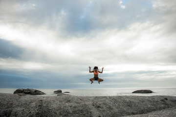 Obraz premium Woman jumping on a rock at sunset on Bakovern Beach, Cape Town.