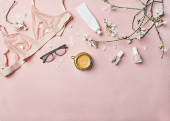 Womans morning rituals concept. Flat-lay of feminine tender powder color lingerie, glasses, cosmetic items, cup of coffee and Spring blossom flowers over pastel pink bed cover, top view, copy space.