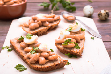 Bruschetta with boiled beans in tomato sauce, quail eggs and parsley on a cutting board