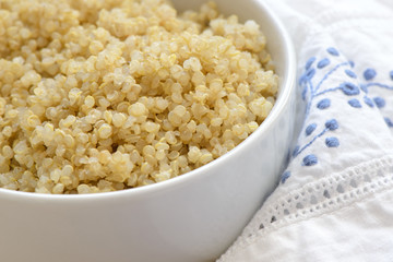 Cooked quinoa in a white bowl on a blue and white napkin