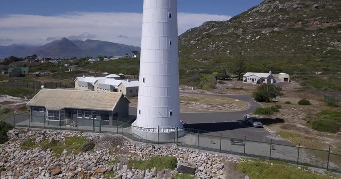 4K high quality aerial video sunny day view of historical Slangkop lighthouse built in 1914 and Kommetjie town in the background near beach at sea shore in Western Cape near Cape Town, South Africa