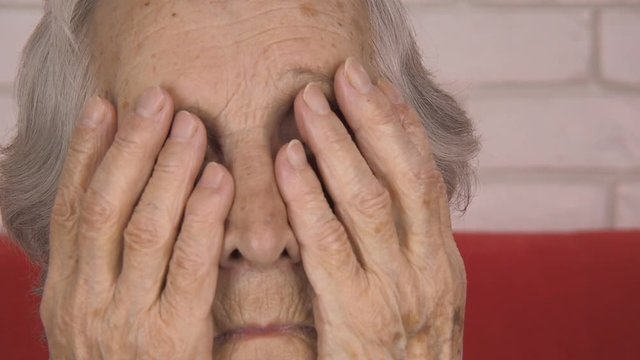 Portrait of an elderly woman. The old woman covers her face with her hands.