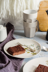 Millet brownie. White plates, cups of coffee and black esspreso maker. White and light blue background. Woolen tapestry.