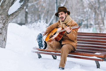cheerful guy playing guitar in park in winter