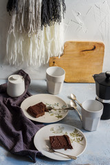 Millet brownie. White plates, cups of coffee and black esspreso maker. White and light blue background. Woolen tapestry.