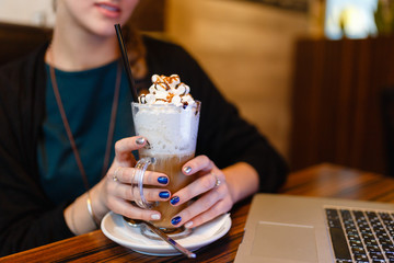 Morning coffee in internet cafe - Beautiful young girl checking news on web and drinking cappuccino. Closeup