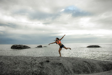Woman jumping on a rock at sunset on Bakovern Beach, Cape Town.