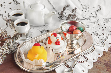 Figures from marzipan in the form of white and yellow chickens on Easter table with coffee cups and pastry eggs in a ceramic white pot.