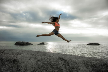 Woman jumping on a rock at sunset on Bakovern Beach, Cape Town.