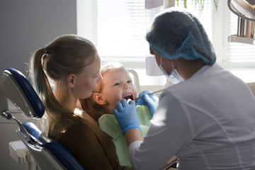 Girl, her mom and the dentist in the dental office, the stomatologist examining the girl using special instruments