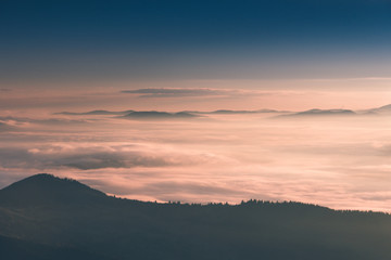 Beautiful landscape in the mountains at sunrise. View of  the foggy hills covered by forest. Retro effect. Traveling concept background.