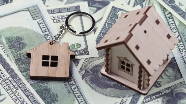 Key and wooden model of house and on dollar banknotes background rotating