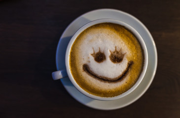 White cup on a saucer with coffee. Coffee with foam and smiley patterns.