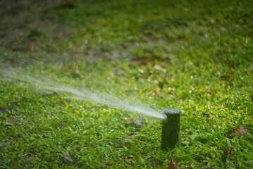 Sprinkler spraying water over green grass, Irrigation system at park.