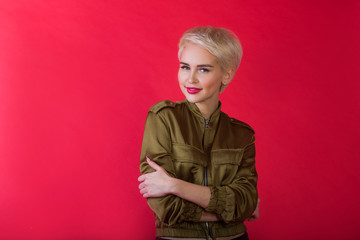 beautiful young girl with a smile and with a short hairdo in a jacket on a red background