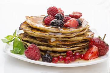 Delicious pancakes with berries and maple syrup on a white background