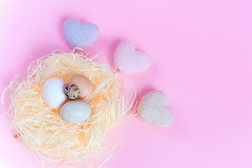 Easter eggs of different colors in a straw nest and decorative textile hearts on a pink background. Top view free copy space. Flat lay. Easter concept.